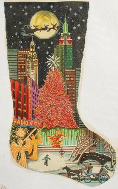 a cross stitch christmas stocking with a city scene and a tree in the center