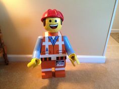 a lego man wearing a hard hat and orange safety vest standing in front of a wall