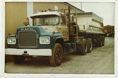 an old mack truck parked in front of a building with a dump truck next to it