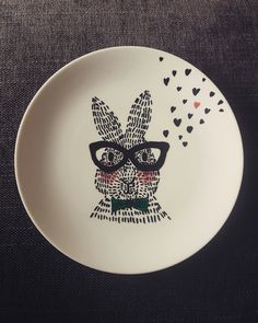 a white plate with a drawing of a rabbit wearing glasses and hearts on the side