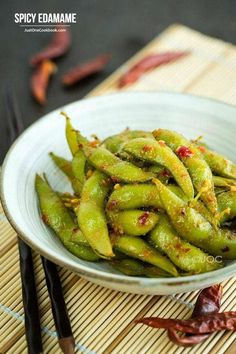 a white bowl filled with green beans sitting on top of a bamboo mat next to chopsticks