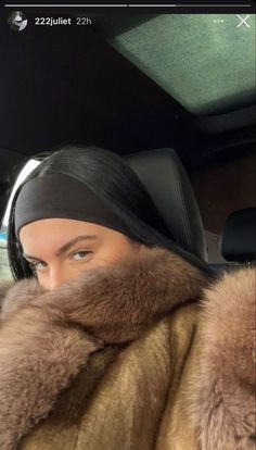 a woman wearing a fur coat and head scarf in the back seat of a car