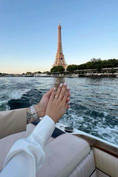 two people holding hands while on a boat in front of the eiffel tower