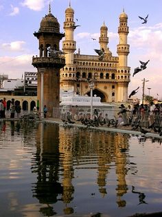 birds are flying over the water in front of a large building with towers and domes