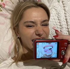 a woman laying in bed taking a selfie with her camera and red nail polish