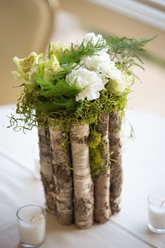 a vase filled with flowers and greenery on top of a table next to two candles