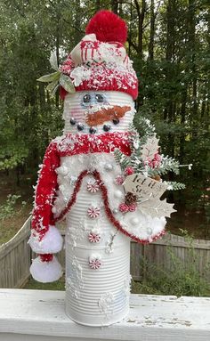 a snowman made out of tin cans is sitting on a porch with trees in the background