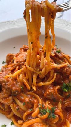 a fork full of spaghetti with meat sauce and parmesan cheese on top is being lifted from a white plate