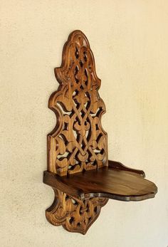 a wooden shelf with an intricate design on the top and bottom, against a white wall