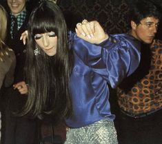 a woman with long black hair dancing in front of other people