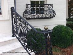 a wrought iron railing with a ball on it in front of a white brick house