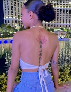 a woman with a tattoo on her back standing in front of a pool at night