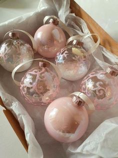 six pink glass ornaments in a box on top of tissue paper with ribbon around them