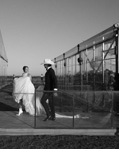 black and white photograph of bride and groom walking in front of glass greenhouse at wedding