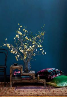 a vase with flowers sitting on top of a wooden table next to a green pillow