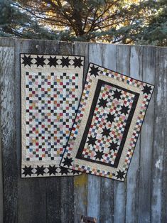 two quilts sitting on top of a wooden fence next to each other in front of a tree