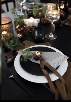 a black and white dinner table setting with candles, napkins, silverware and greenery