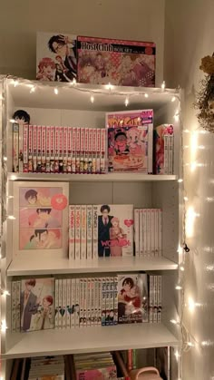 a book shelf filled with lots of books next to a wall covered in fairy lights