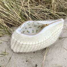 a white purse sitting on top of a sandy beach next to some tall dry grass