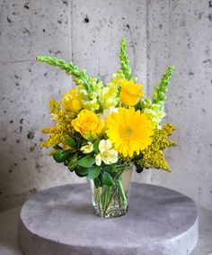 a vase filled with yellow flowers sitting on top of a round gray table next to a wall