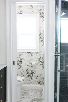 a white toilet sitting next to a shower in a bathroom under a window covered in black and white wallpaper