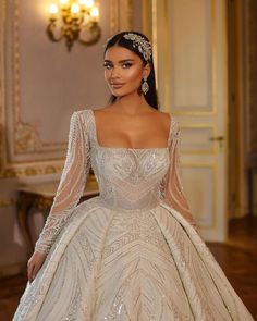 a woman in a wedding dress with long sleeves and beading on her head, standing next to a chandelier