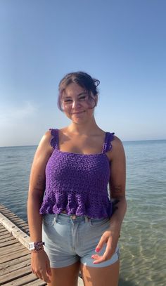 a woman standing on a dock next to the ocean with her hands in her pockets