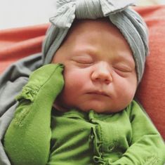 a newborn baby wearing a green outfit and a gray headband