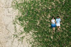 an aerial view of two people standing in the sand with flowers growing all around them