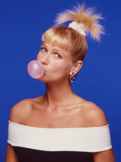 a woman blowing bubbles with her hair in a bun on top of her head, against a blue background