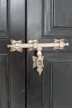 a close up of a metal door handle on a black door with wood paneling