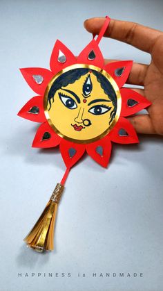 a hand holding a red and gold paper decoration with a yellow face on the center