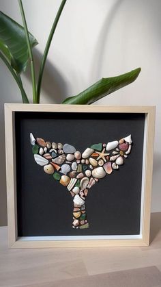 an art piece made out of seashells in a wooden frame on a table next to a potted plant