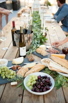 people are sitting at an outdoor table with food and wine bottles on it, along with glasses of wine