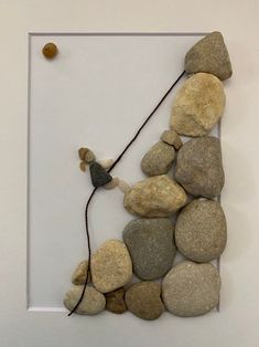 a white frame with some rocks and a string attached to the back of it that is hanging on a wall