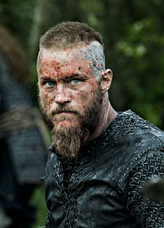 a close up of a man with blue eyes and a beard covered in mud wearing armor