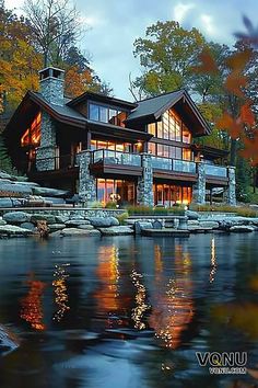 A rustic lakeside lodge with stone accents, large windows, and warm interior lighting, set against a backdrop of autumn foliage and reflecting beautifully on the calm water, creating a serene and inviting atmosphere. 3 Story Lake House, Lake Houses Exterior Big Windows, Huge Lake House Exterior, Lake View Homes Big Windows, Small Lake House Plans Big Windows, Lakeside Lodge