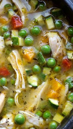 a pot filled with chicken and vegetables on top of a table next to a wooden spoon