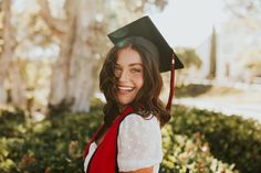 a woman in a graduation cap and gown smiles at the camera while wearing a red vest