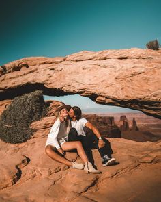 two people are sitting on the rocks in front of an arch that is shaped like a rock