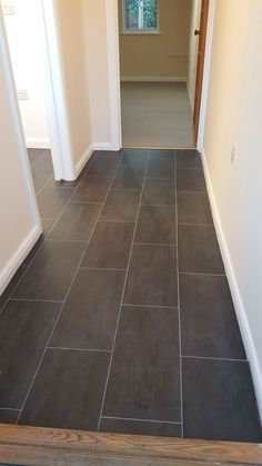 an empty hallway with tile flooring and wooden door way leading to another room in the house