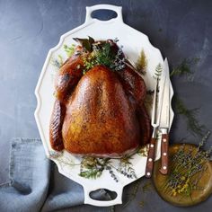 a roasted turkey on a platter next to a knife, fork and sprig of herbs