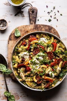 a bowl filled with pasta salad on top of a wooden cutting board