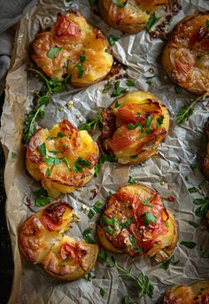 baked potatoes topped with tomatoes and herbs on aluminum foil lined up on a sheet of wax paper