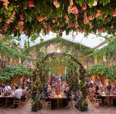 an outdoor dining area with flowers and greenery on the ceiling, surrounded by tables