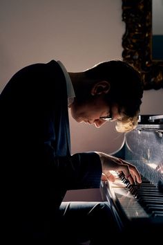 a young man is playing the piano in his living room at night time with light coming from behind him