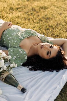 a woman laying on top of a white blanket next to a bottle of wine and flowers