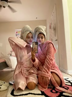 two women in pink robes taking a selfie with their cell phone while sitting on the floor