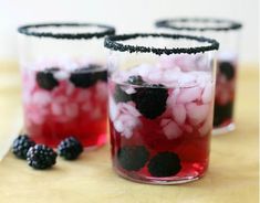 three glasses filled with blackberries and raspberries on top of a wooden table