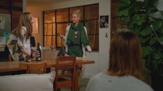 two women standing in a living room talking to each other while one woman holds a wine bottle